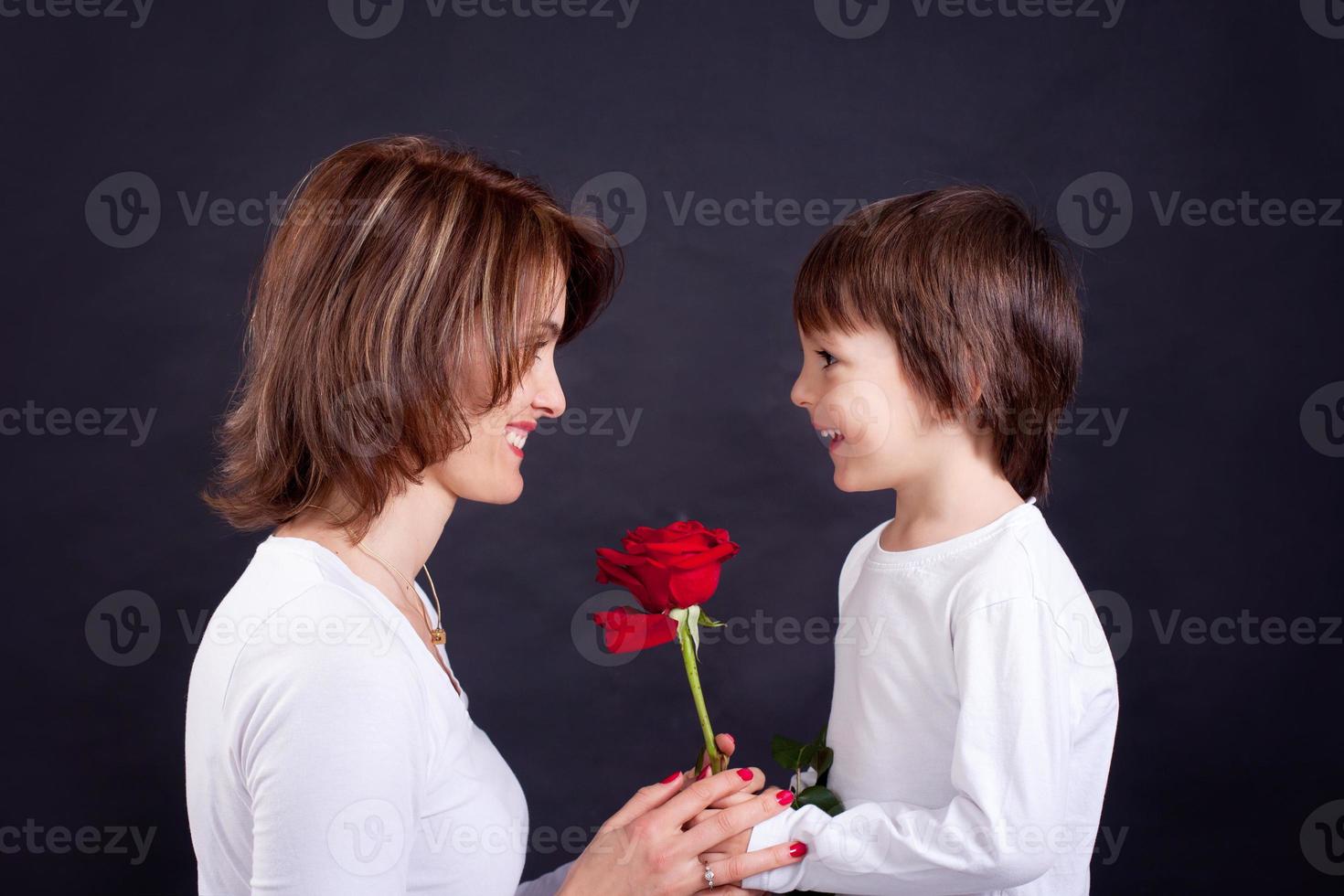 Junge, die seiner Mutter eine wunderschöne rote Rose gibt foto