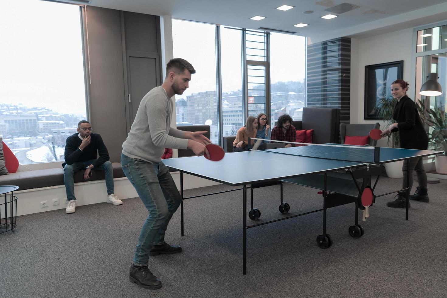 Junger Start-up-Geschäftsmann und -frau, die Tischtennis in modernen kreativen Büroräumen spielen, treffen sich und Brainstorming im Hintergrund foto