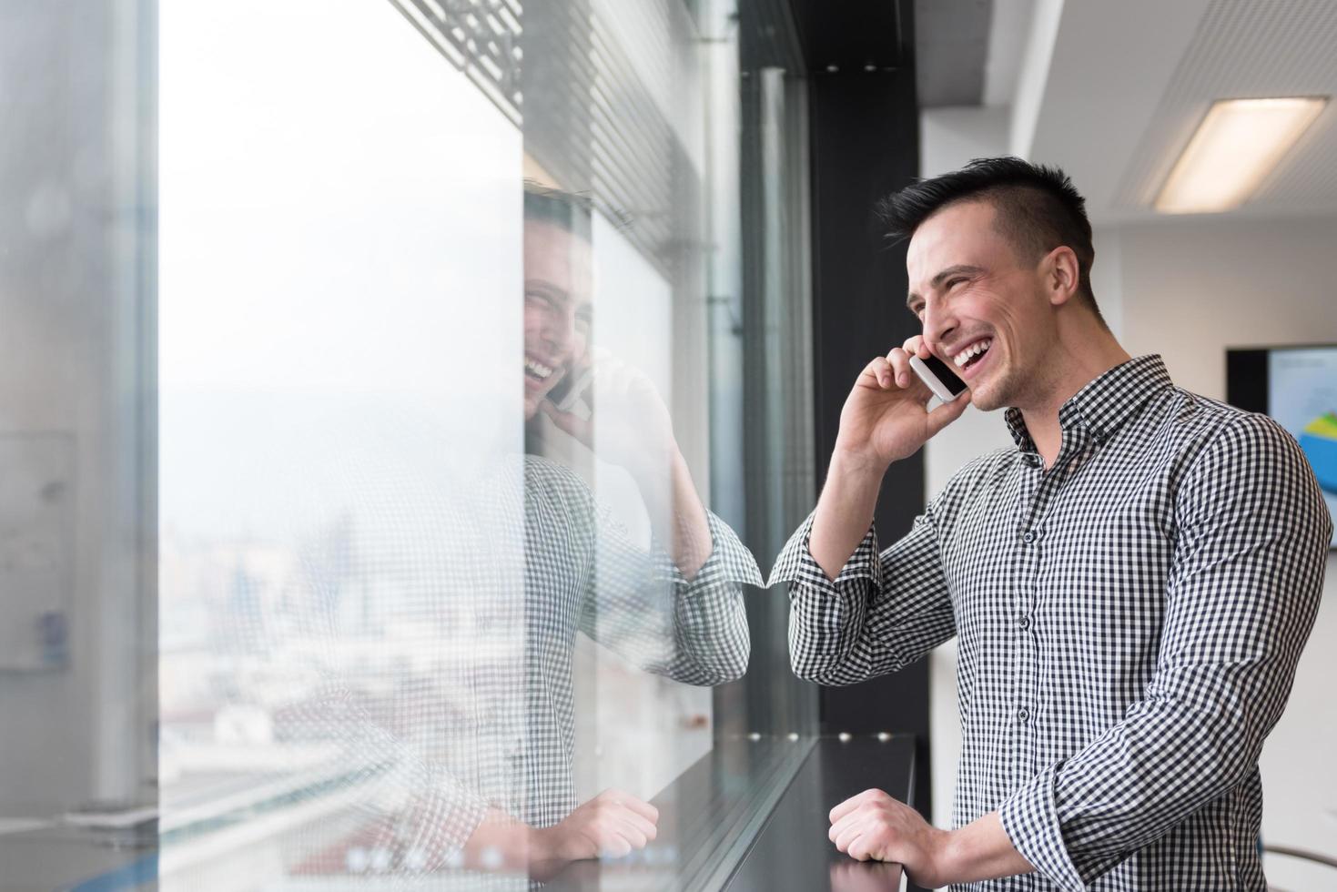 Junger Geschäftsmann, der im Büro am Smartphone spricht foto