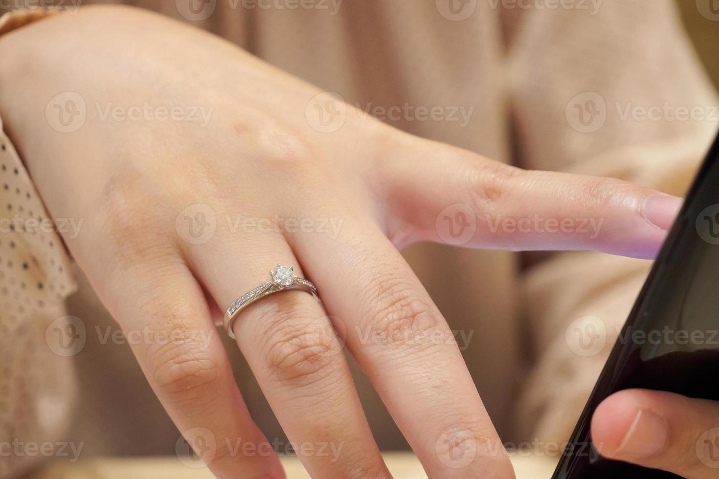 Schließen Sie den Diamantring am Finger der Frau mit dem Smartphone foto