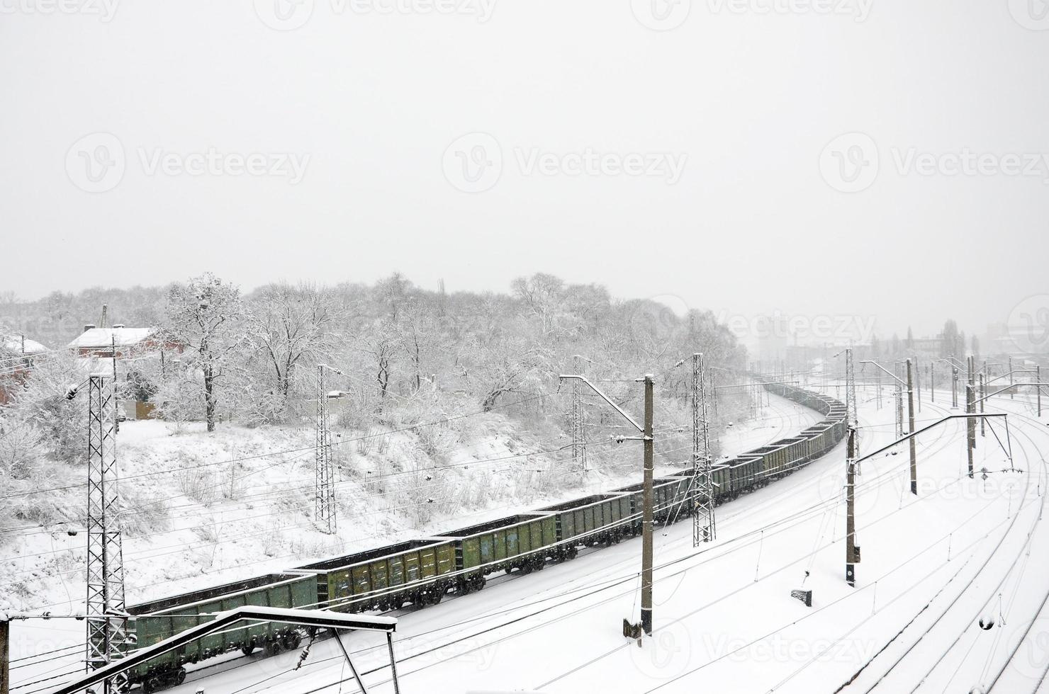 ein langer zug von güterwagen bewegt sich entlang der bahngleise. Eisenbahnlandschaft im Winter nach Schneefall foto