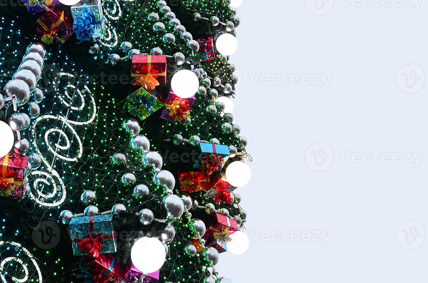 ein Fragment eines riesigen Weihnachtsbaums mit vielen Ornamenten, Geschenkboxen und leuchtenden Lampen. Foto einer geschmückten Weihnachtsbaumnahaufnahme mit Kopienraum