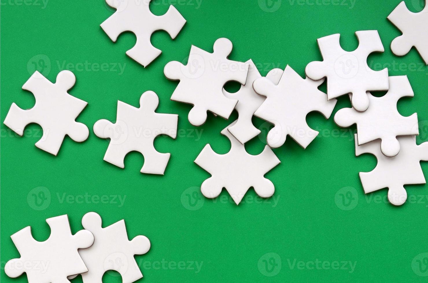 Ein Haufen ungekämmter Elemente eines weißen Puzzles liegt auf dem Hintergrund einer grünen Oberfläche. texturfoto mit kopierraum für text foto