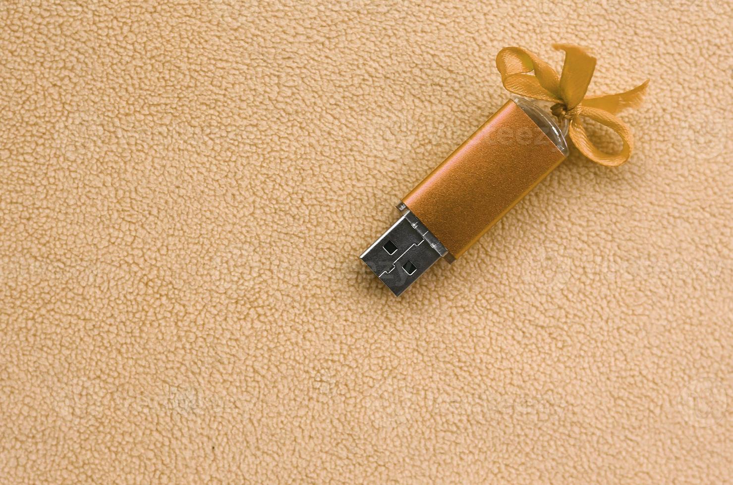 Orangefarbene USB-Flash-Speicherkarte mit blauer Schleife liegt auf einer Decke aus weichem und pelzigem, hellorangefarbenem Fleece-Stoff. klassisches weibliches Geschenkdesign für eine Speicherkarte foto