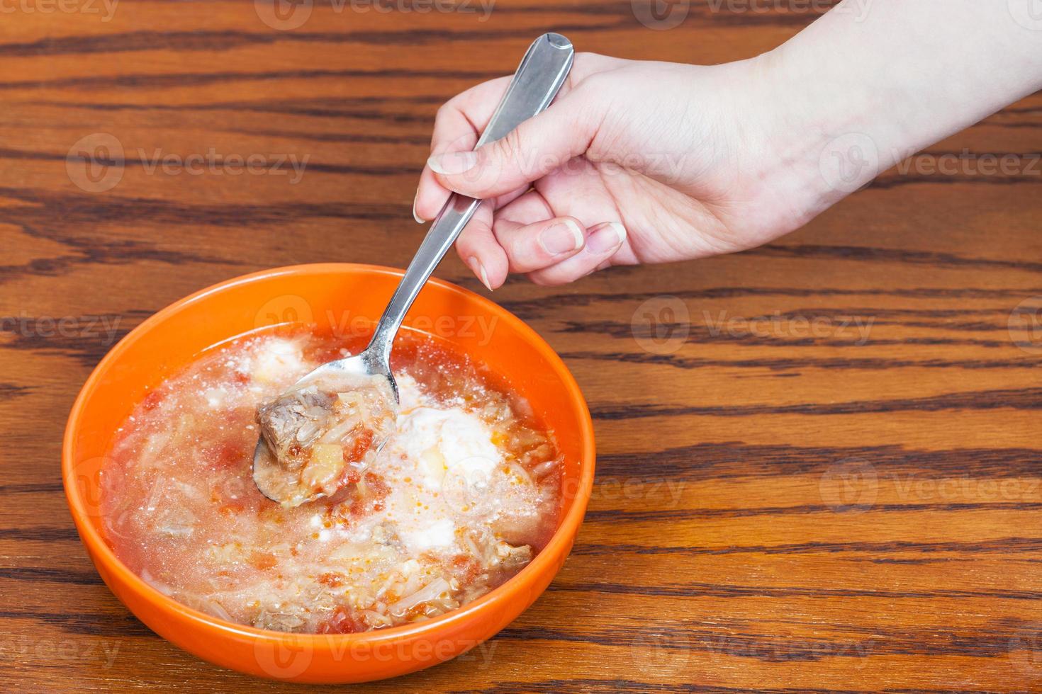 Hand hält Löffel mit Kohlsuppe über Schüssel foto