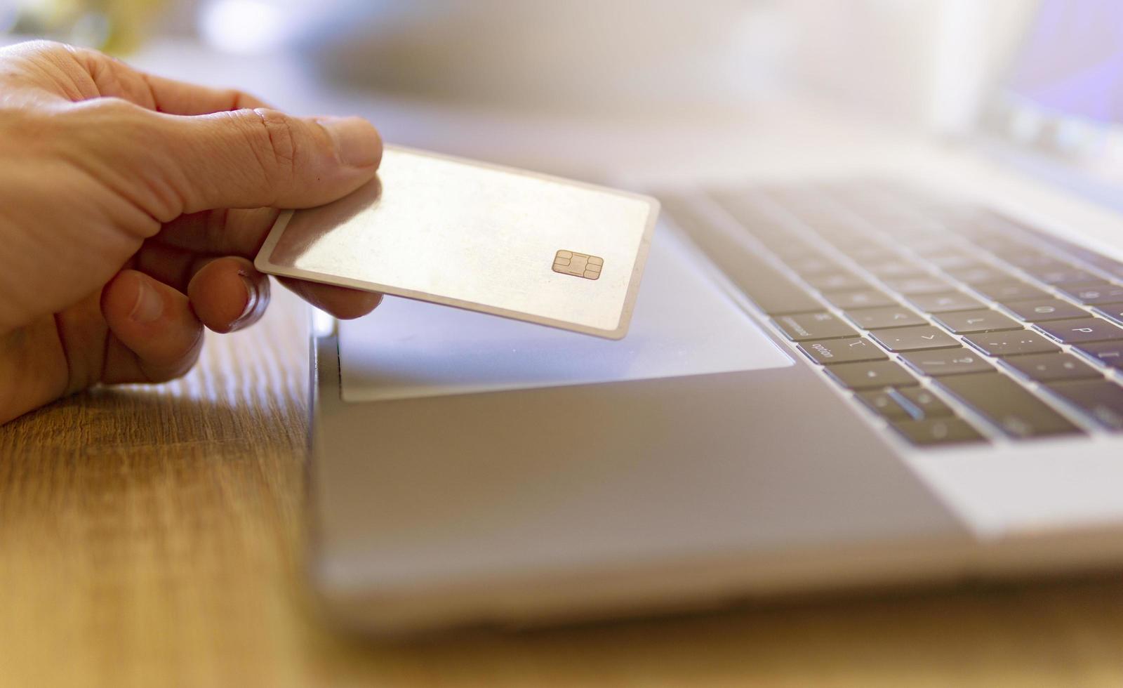 Hand hält goldene Kreditkarte neben Laptop foto