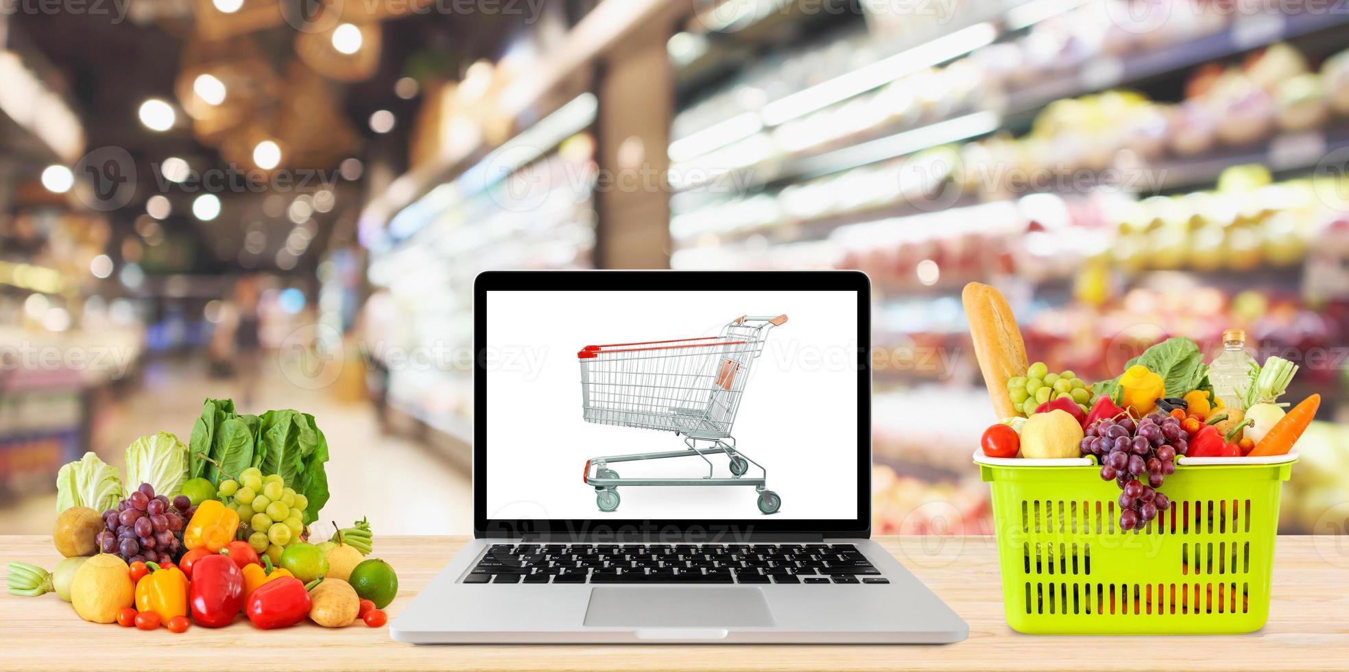 Supermarktgang verschwommenen Hintergrund mit Laptop-Computer und Einkaufswagen auf Holztisch Lebensmittelgeschäft Online-Konzept foto