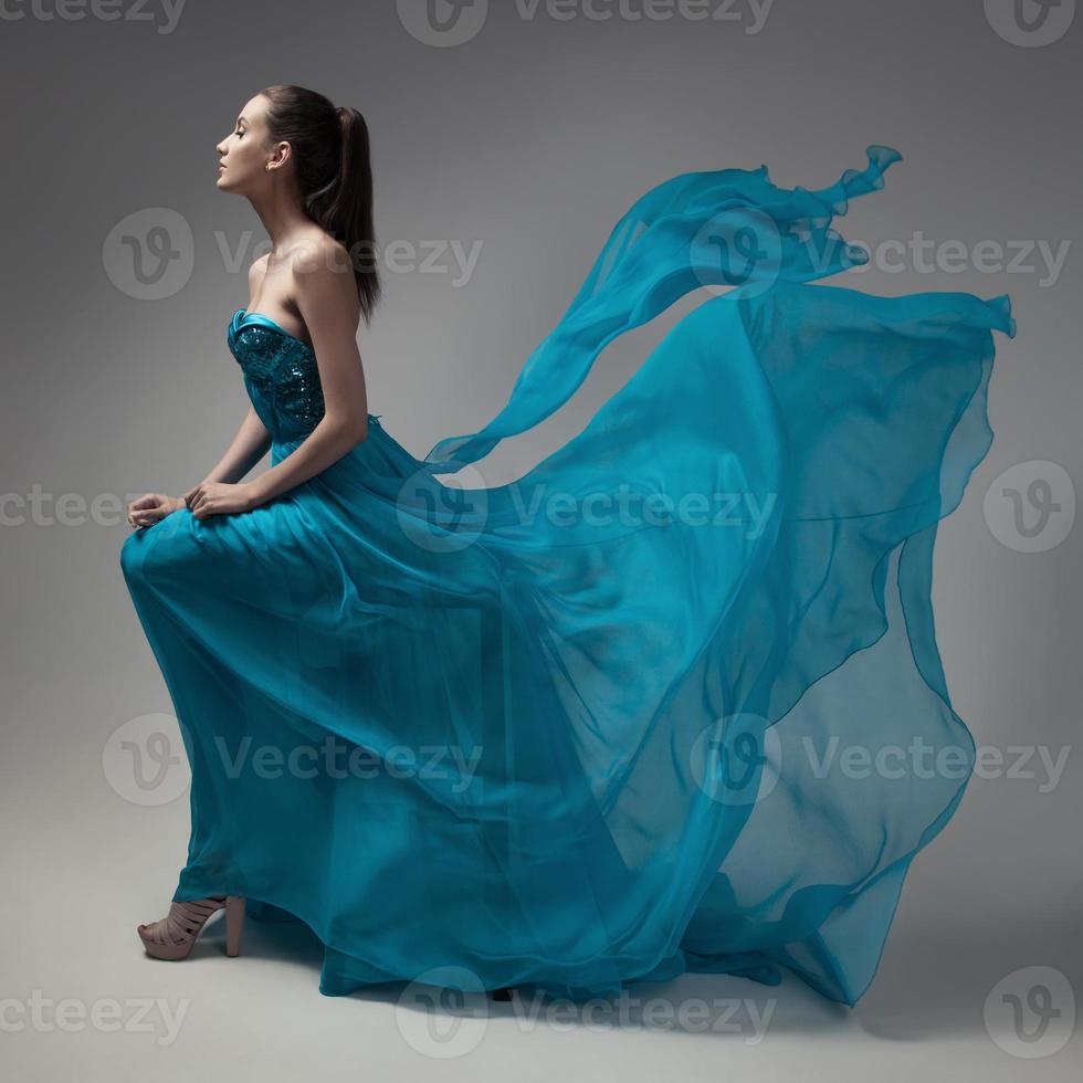 Modefrau im flatternden blauen Kleid. grauer Hintergrund. foto