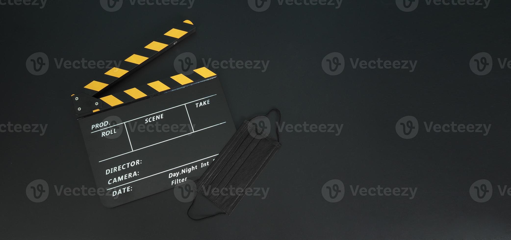 gelbe klappe oder filmtafel mit schwarzer gesichtsmaske oder medizinischer maske isoliert. es wird in der film-, filmproduktions- und kinoindustrie auf schwarzem hintergrund verwendet. covid-19 oder soziales distanzkonzept. foto