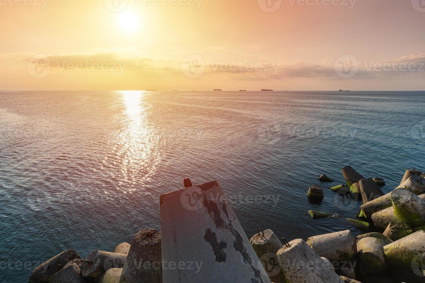 schöne sonnenuntergang seelandschaft. Reiseträume und Motivation. Wellenbrecher Tetrapoden am Ufer des Piers. Frachtschiffe am Horizont. foto