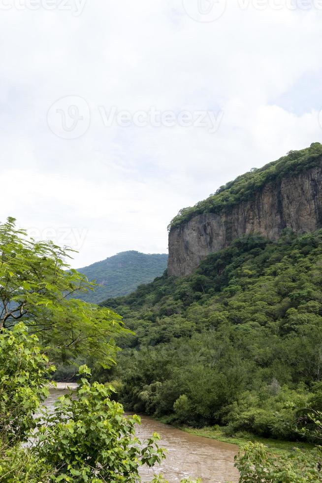 dreckiger fluss, gesehen durch die huentitan-schlucht in guadalajara, grüne vegetation, bäume, pflanzen und berge, mexiko foto