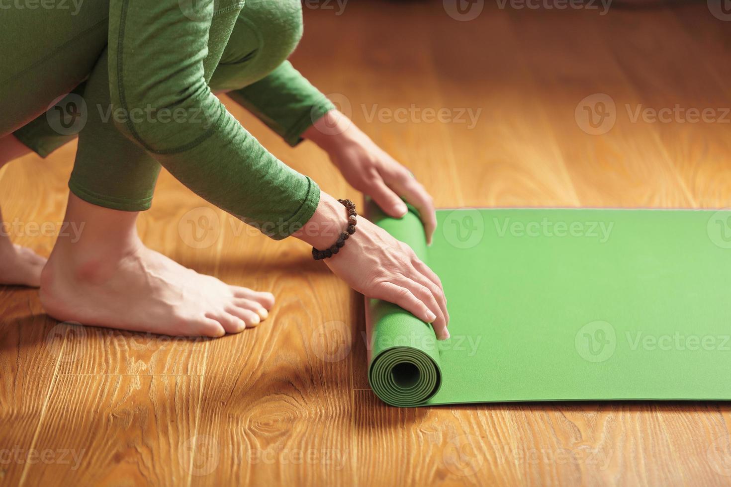 Eine Frau rollt vor einem Yoga-Kurs eine grüne Matte aus foto