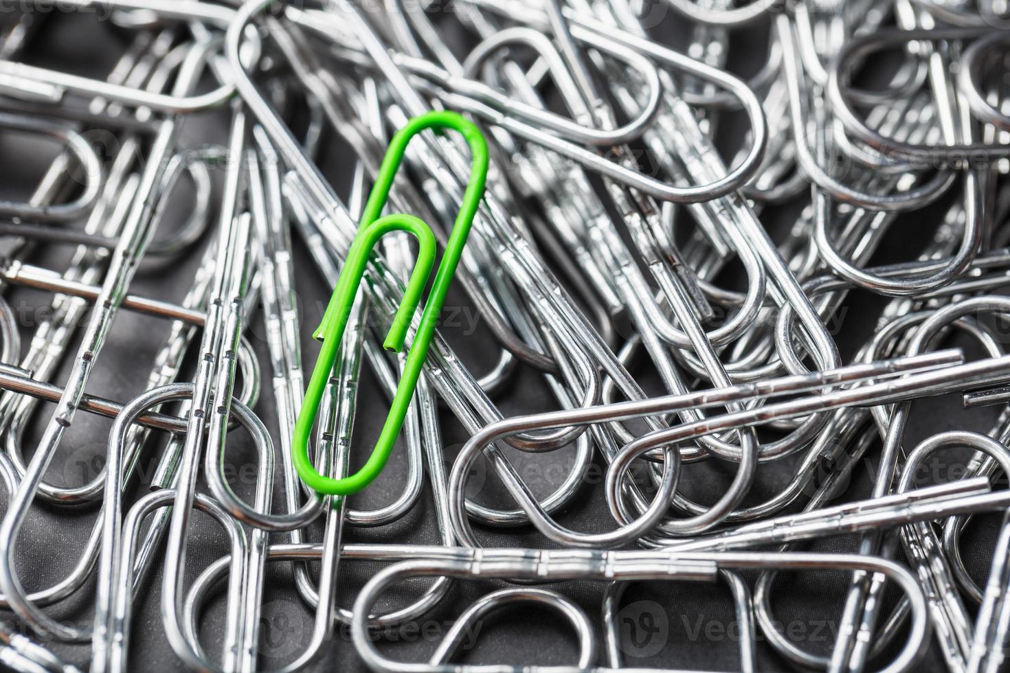 Die grüne Büroklammer hebt sich von einem strukturierten Hintergrund aus silbernen Büroklammern ab foto