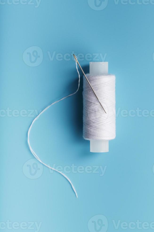 ein Knäuel aus weißem Faden mit einer Nadel auf blauem Hintergrund foto