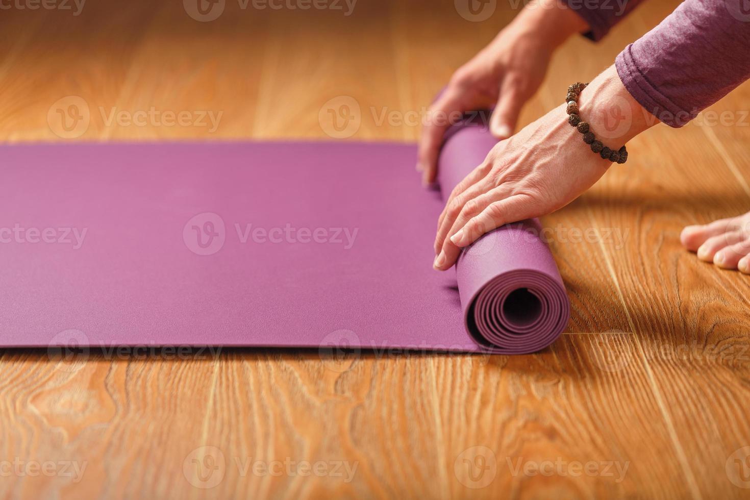 Ein Mädchen legt vor einer Trainingspraxis zu Hause auf einem Holzboden eine lila Yogamatte aus. foto