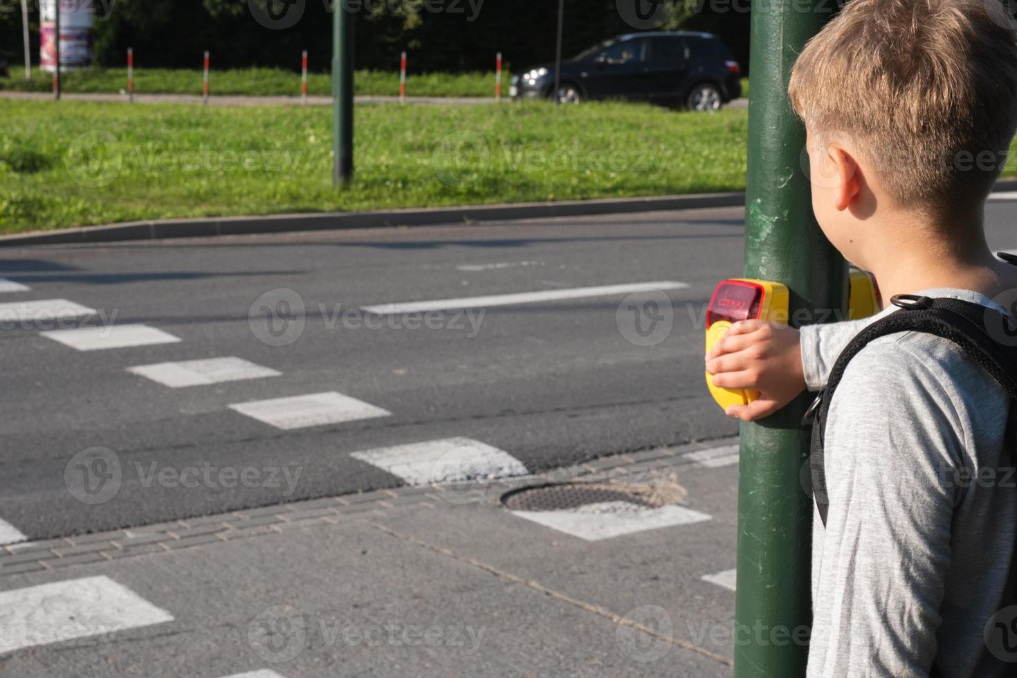 Schuljunge in der Nähe von Fußgängerüberweg und drückt bei Bedarf gelbes Gerät mit Knopf an der Ampel foto