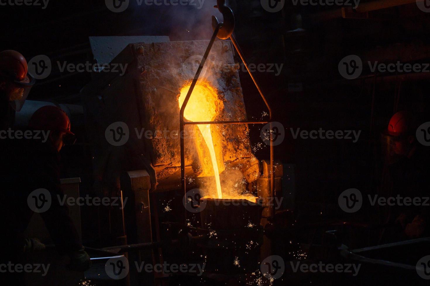 Drei Arbeiter füllen Pfanne mit geschmolzenem Stahl foto