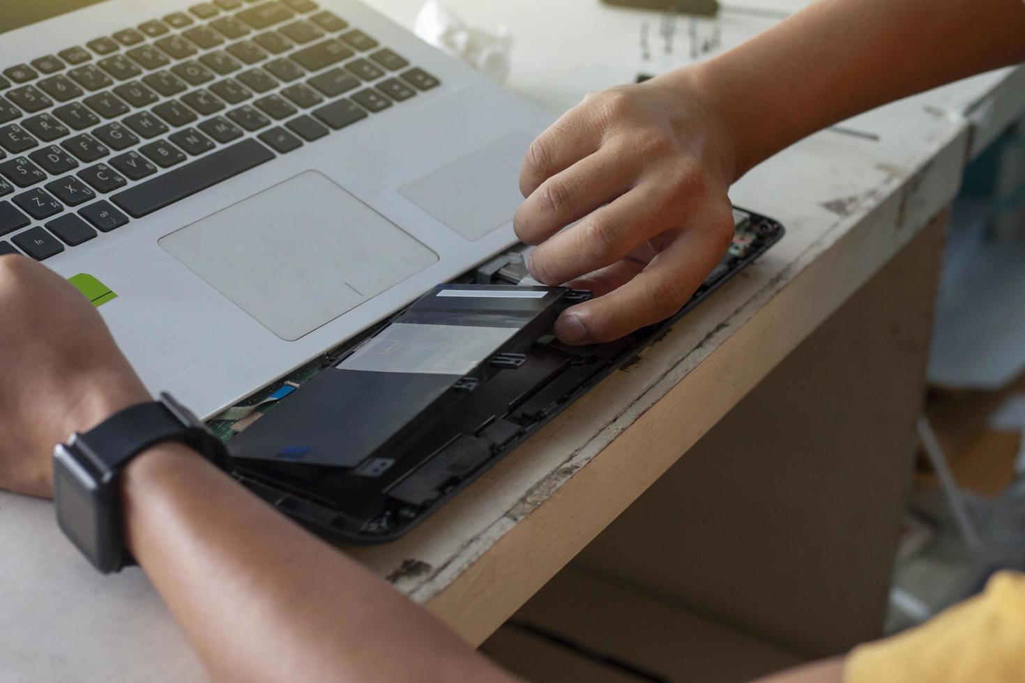 der techniker wechselt die batterien, um den laptop mit thailändischer tastatur zu reparieren. foto