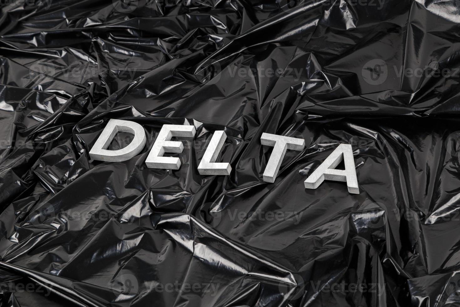 das wort delta mit silbernen metallbuchstaben auf zerknittertem schwarzem plastiktütenhintergrund in diagonaler perspektive foto