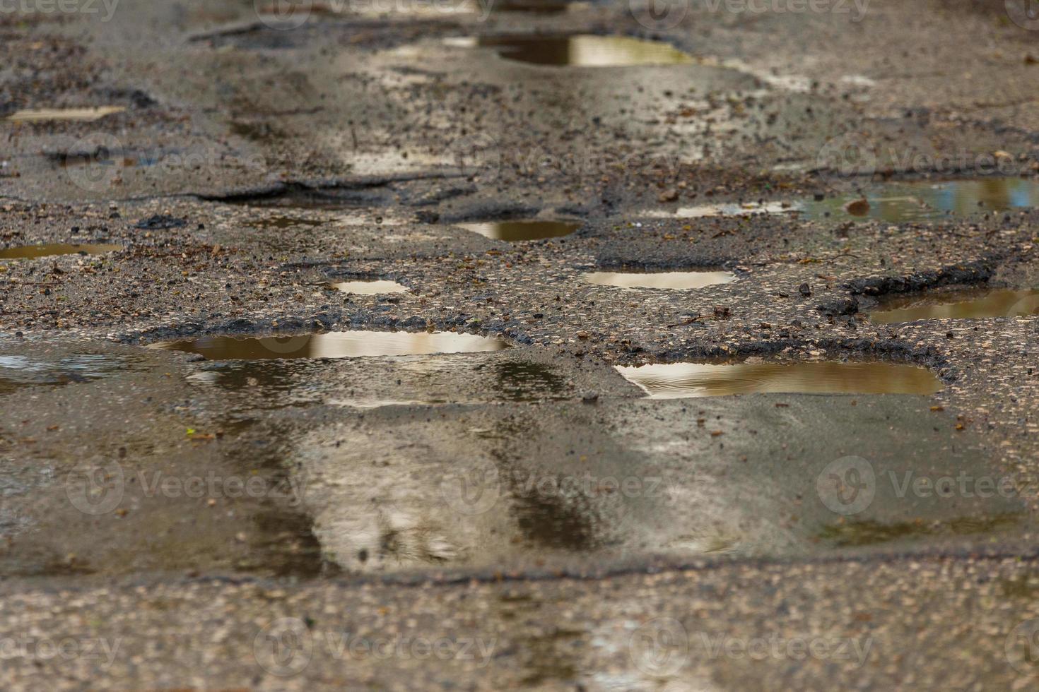 schlaglöcher und pfützen auf schlecht gebrochener nasser asphaltstraße nach regen foto