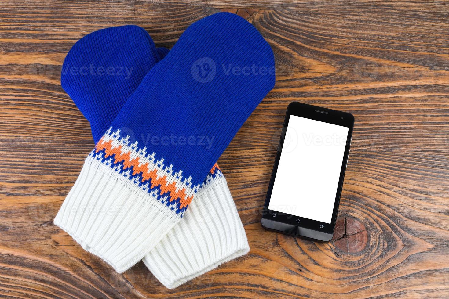 blaue und weiße gestrickte Fäustlinge mit Handy auf Holzhintergrund foto