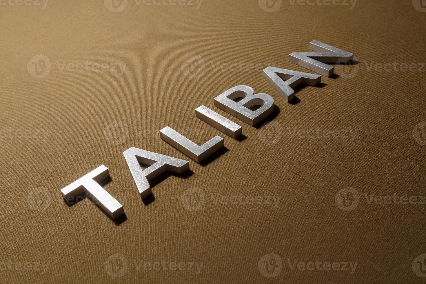 das wort taliban mit silbernen metallbuchstaben auf grobem khakifarbenem canvas-stoff foto