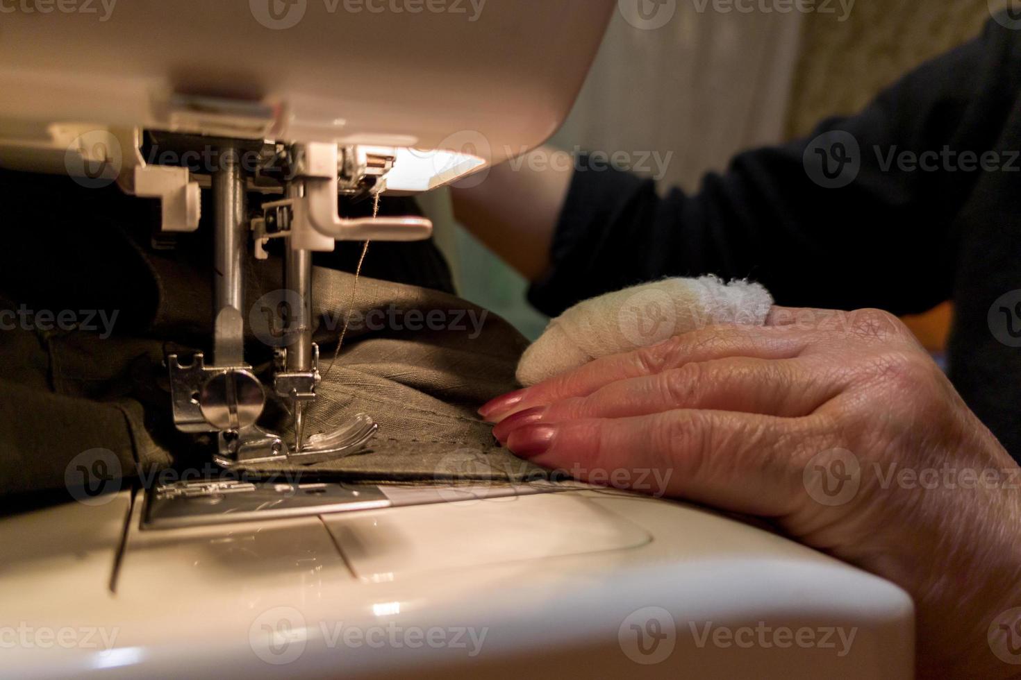 Eine Hand alter Frauen mit bandagiertem Finger näht mit einer Nähmaschine foto