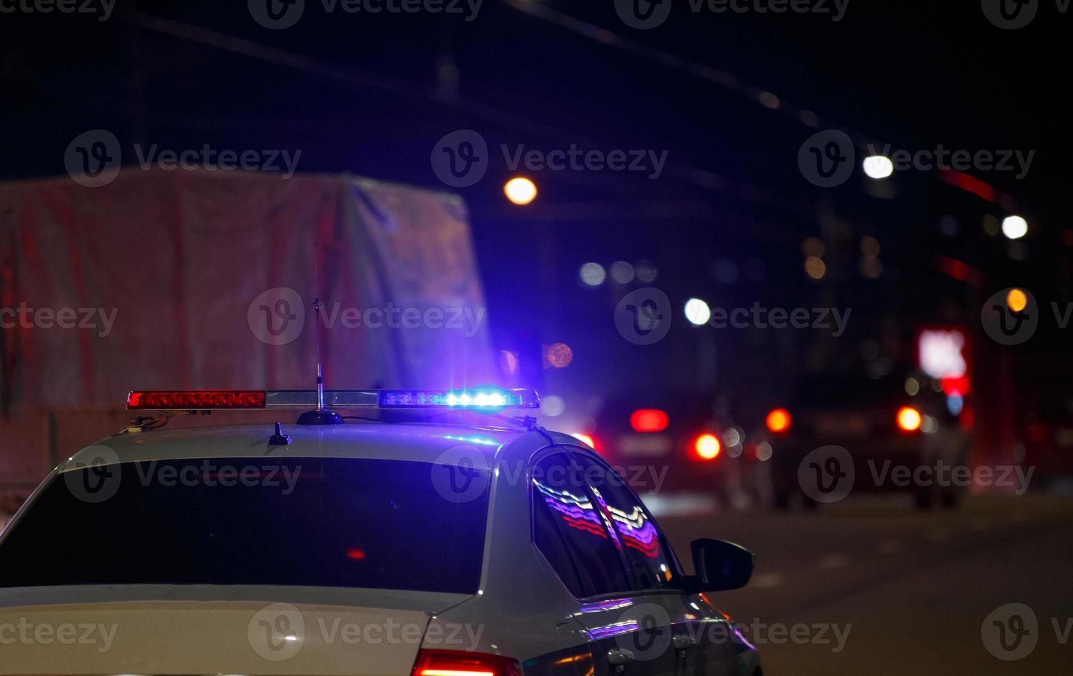 Unrekonsierbares Straßenpolizeiauto mit eingeschaltetem rotem und blauem Sirenenlicht auf dem Dach auf der nächtlichen Stadtstraße foto