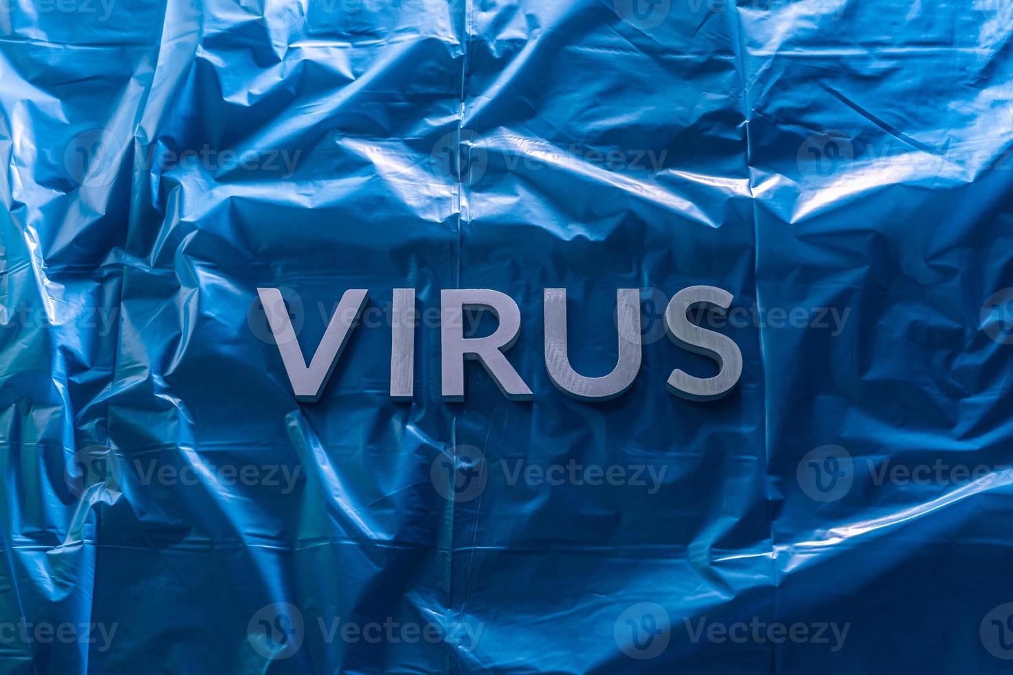 Das Wort Virus mit silbernen Metallbuchstaben auf zerknitterter blauer Plastikfolie mit dramatischem Licht foto