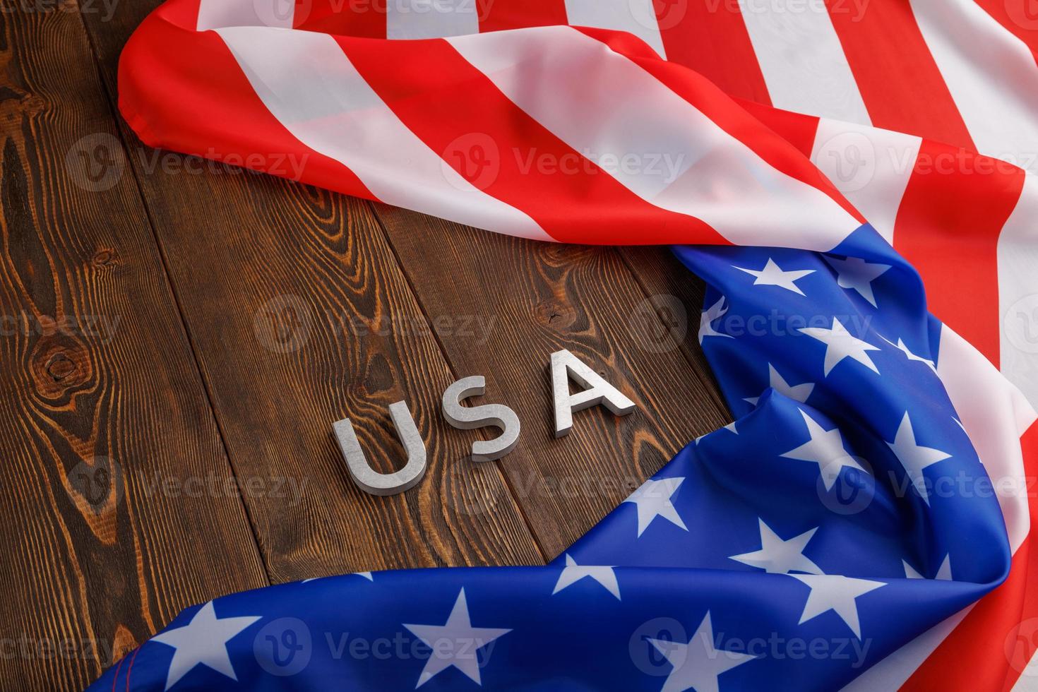 das wort usa mit silbernen metallbuchstaben auf einer holzbrettoberfläche, umgeben von einer zerknitterten flagge der vereinigten staaten von amerika foto