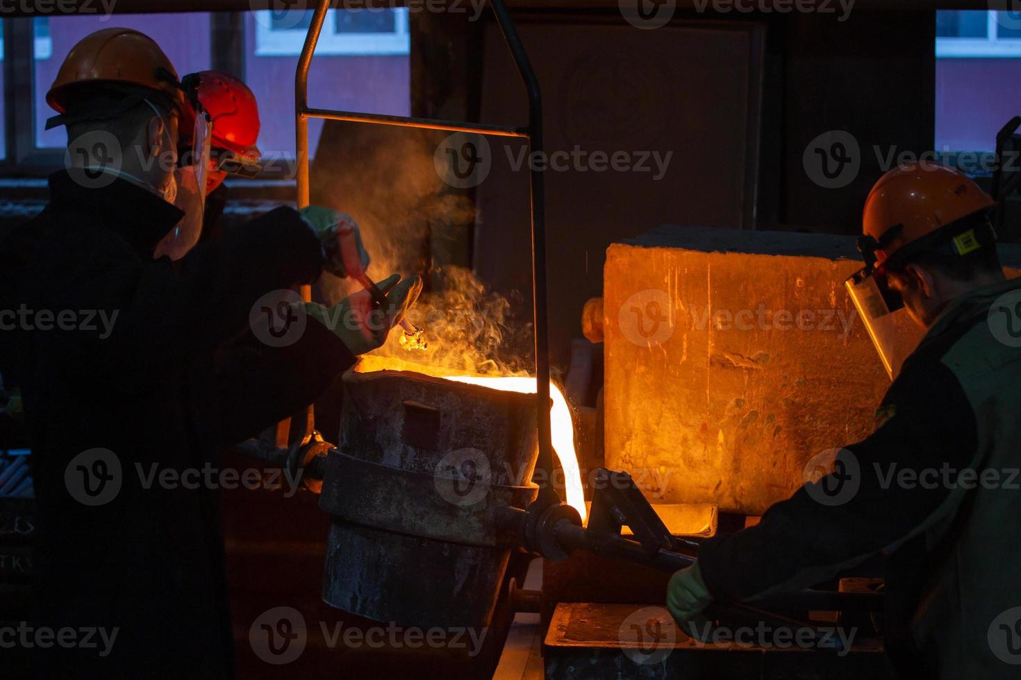 Drei Arbeiter mit Pfanne gießen geschmolzenen Stahl in Form foto