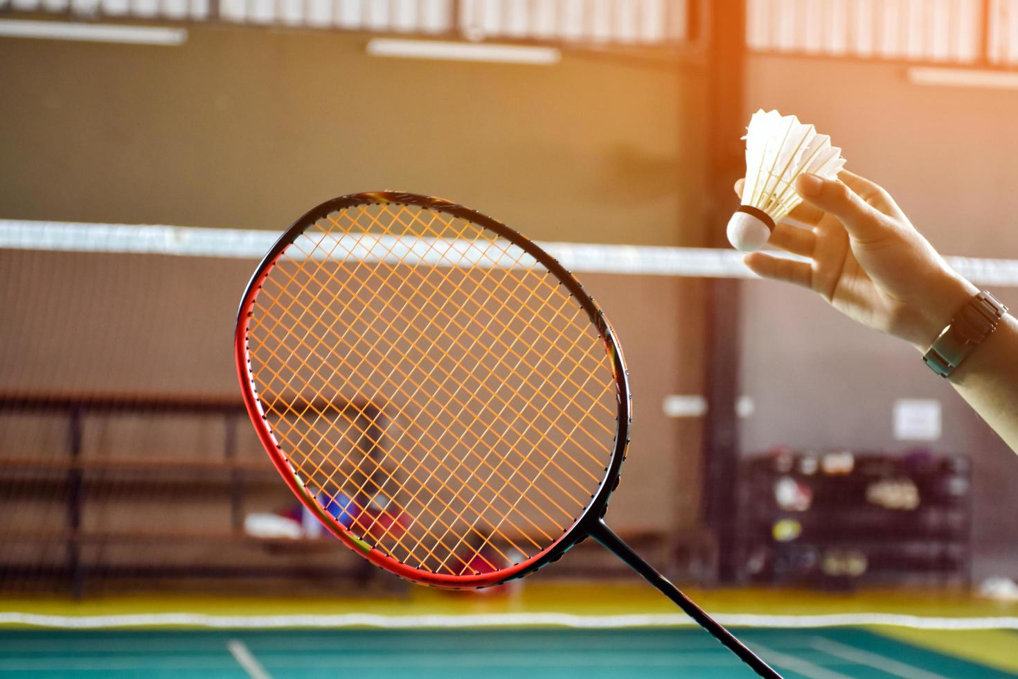 Badmintonspieler hält Schläger und Federball mit weißer Creme vor das Netz, bevor er ihn auf einer anderen Seite des Platzes serviert. foto