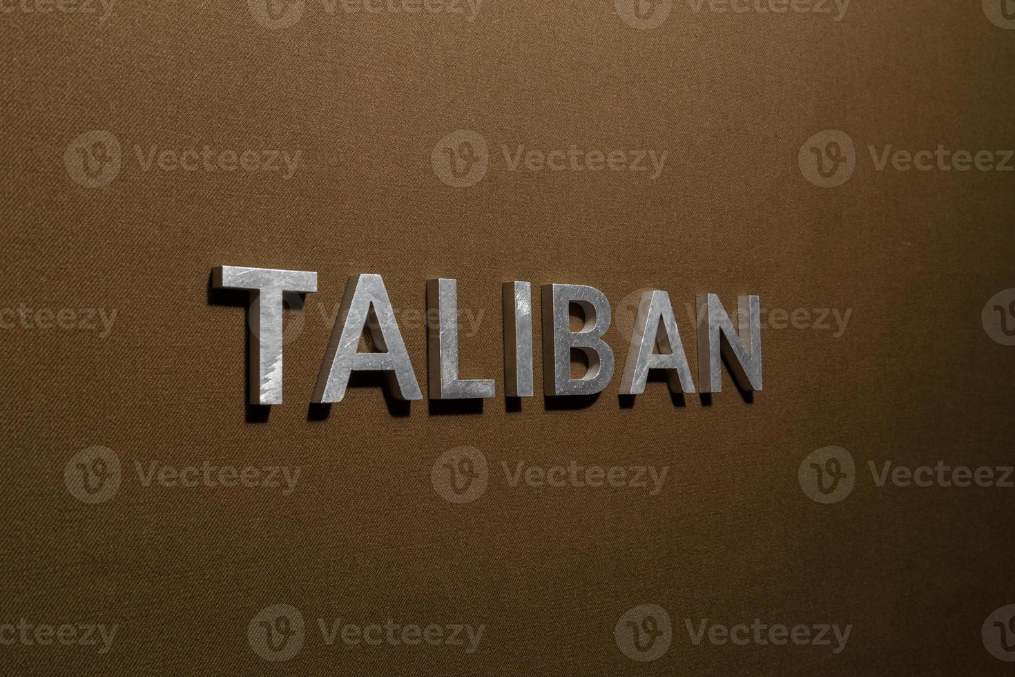 das wort taliban mit silbernen metallbuchstaben auf grobem khakifarbenem canvas-stoff foto