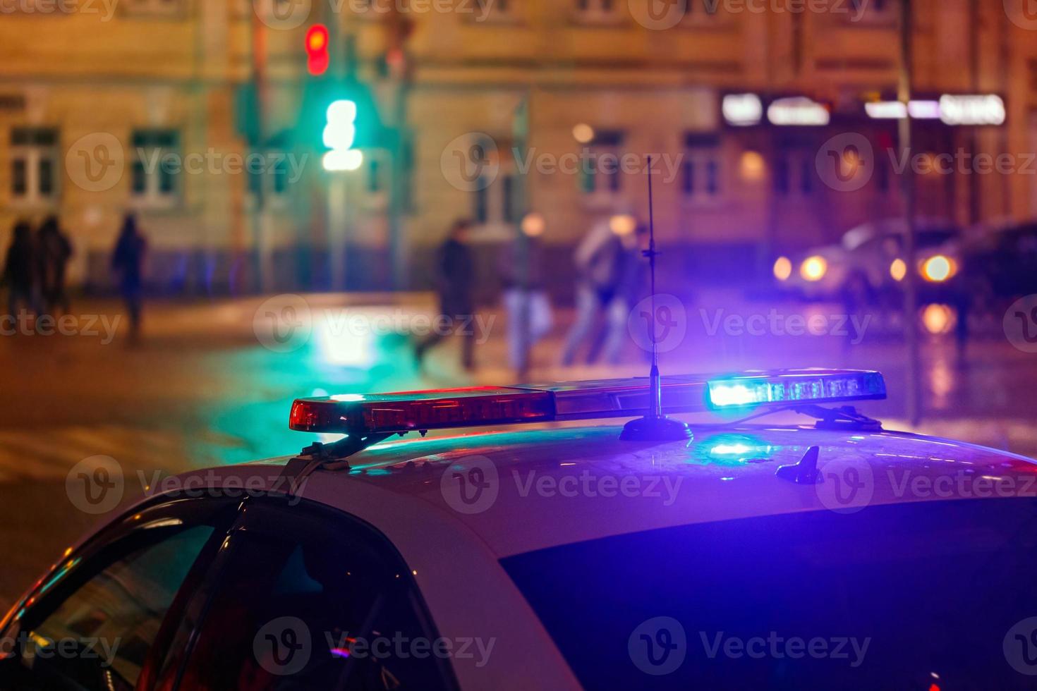 Nachtpolizeiauto leuchtet in der Stadtstraße mit verschwommenen Fußgängern, die die Straße im Hintergrund überqueren foto