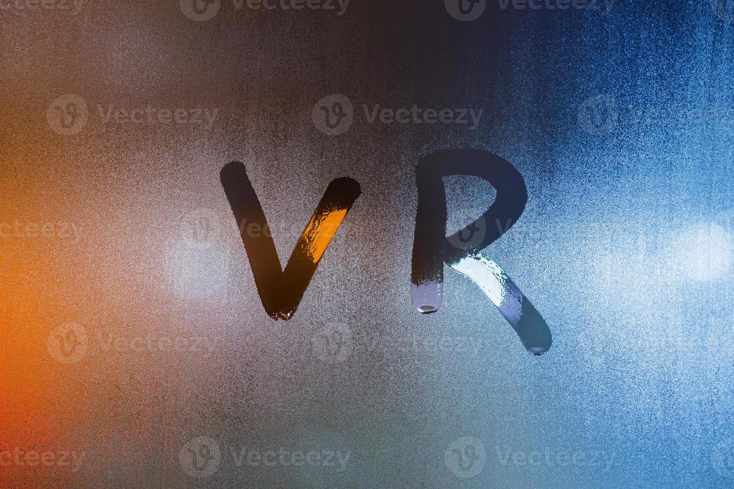 Das Wort vr - Virtual Reality - geschrieben mit dem Finger auf nassem Glas mit verschwommenen Lichtern im Hintergrund foto