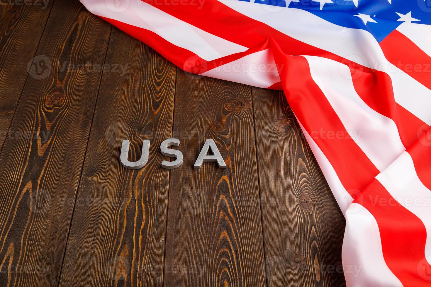 das wort usa mit silbernen metallbuchstaben auf holzbrettoberfläche mit zerknitterter flagge der vereinigten staaten von amerika oben rechts foto