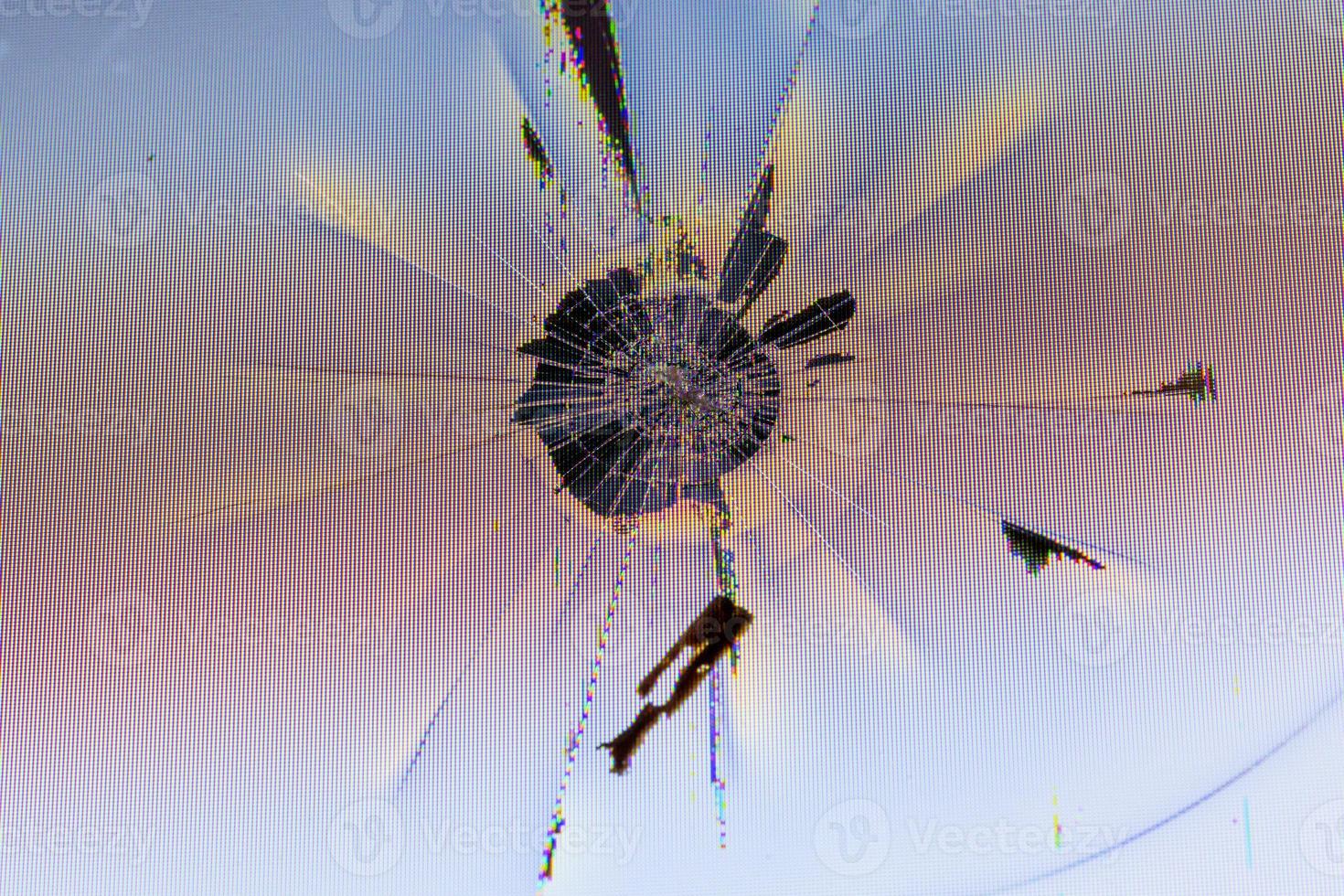 Nahaufnahme einer physisch beschädigten LCD-Bildschirmoberfläche mit Aufprallstelle, radialen Rissen, Pixelgitterlecks und Verfärbungen foto