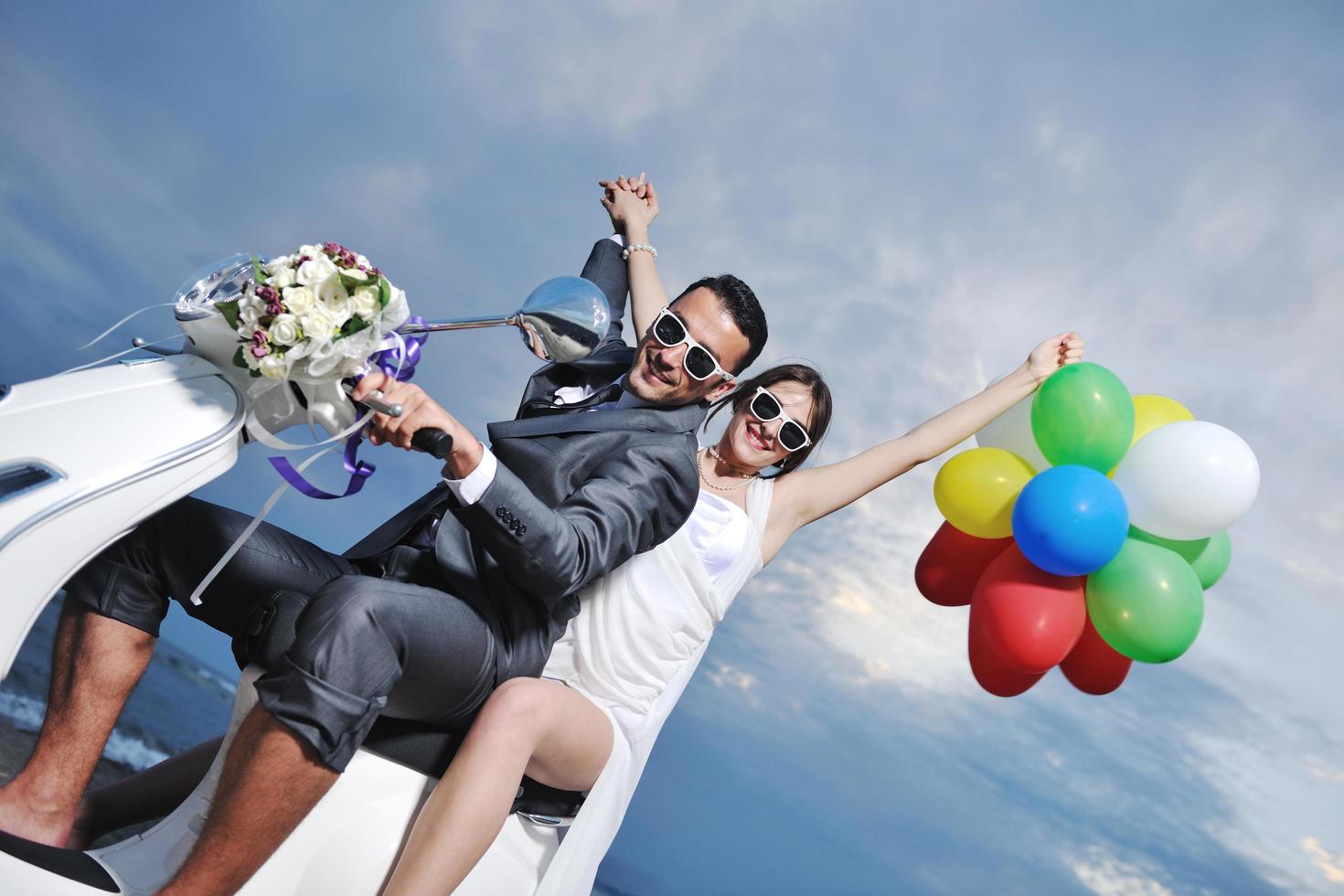 Gerade verheiratetes Paar am Strand fährt weißen Roller foto