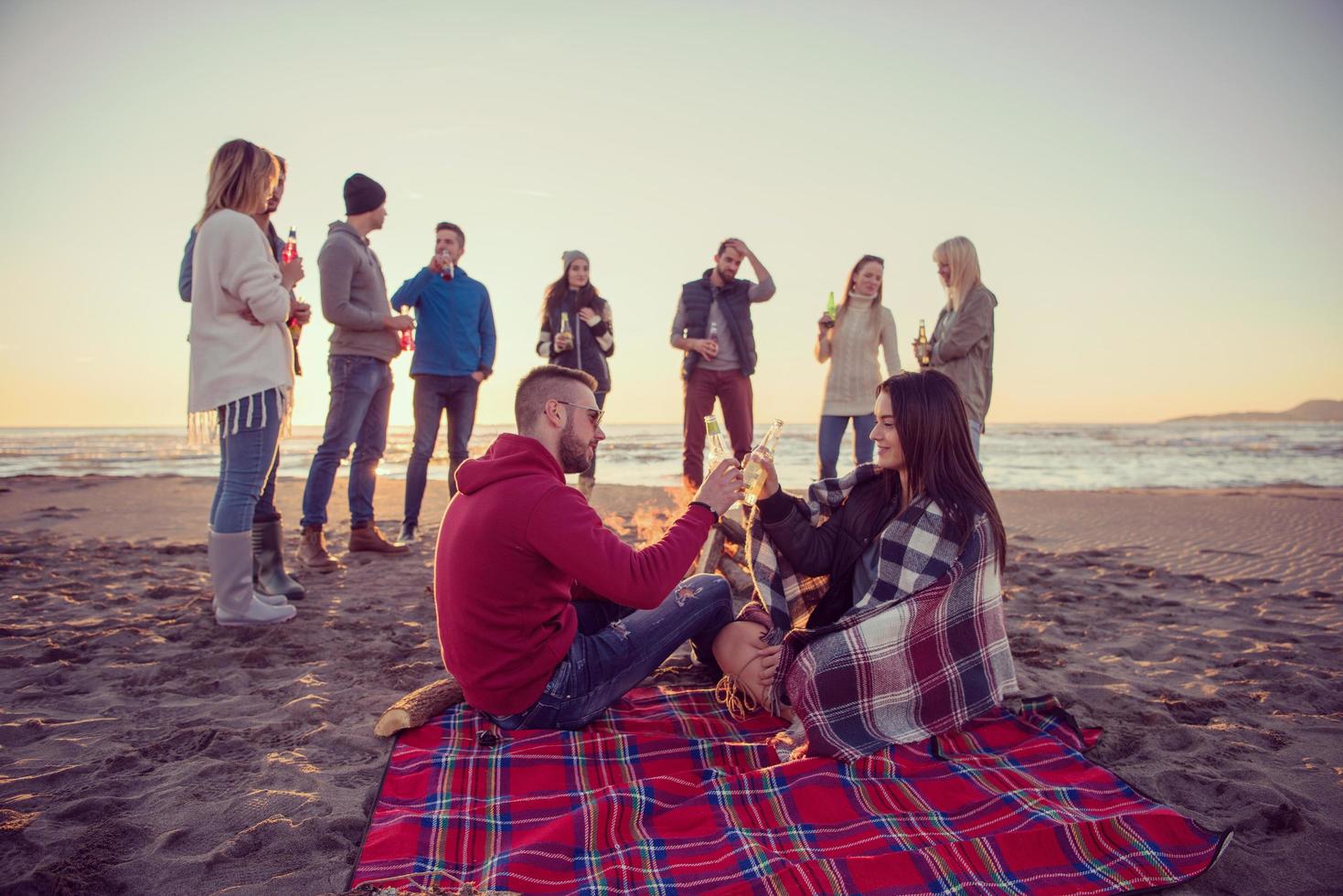 Paar genießt mit Freunden den Sonnenuntergang am Strand foto