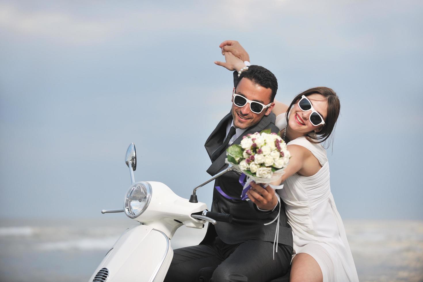 Gerade verheiratetes Paar am Strand fährt weißen Roller foto