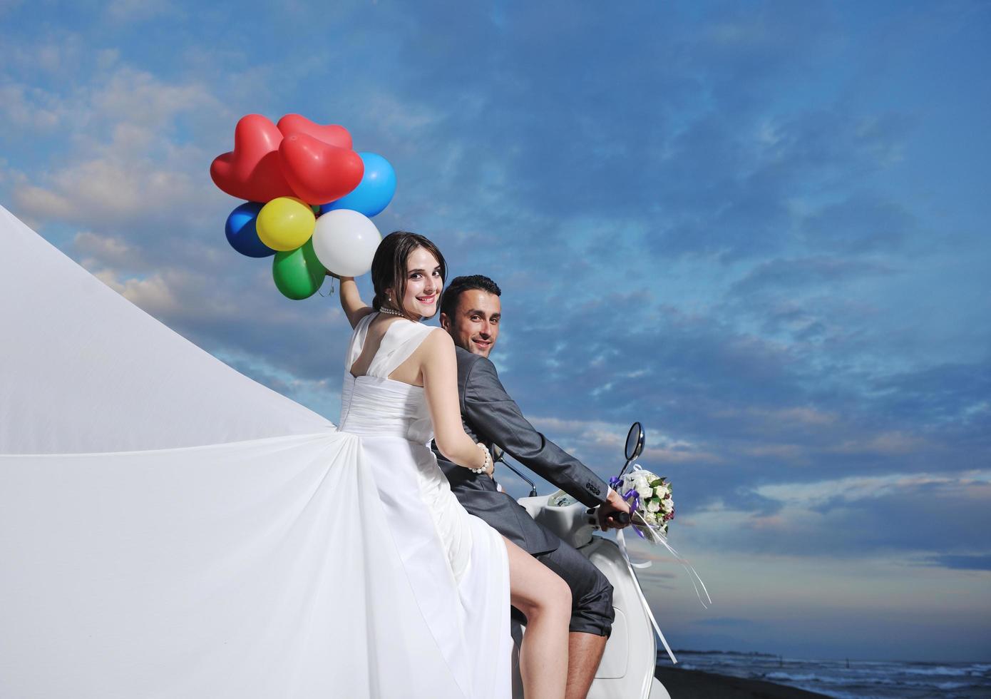 Gerade verheiratetes Paar am Strand fährt weißen Roller foto