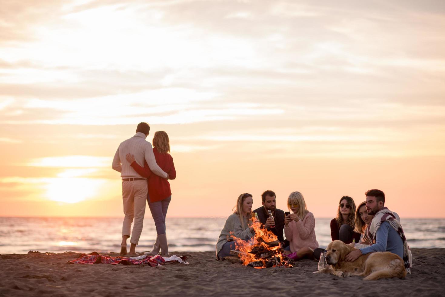 Paar genießt mit Freunden den Sonnenuntergang am Strand foto