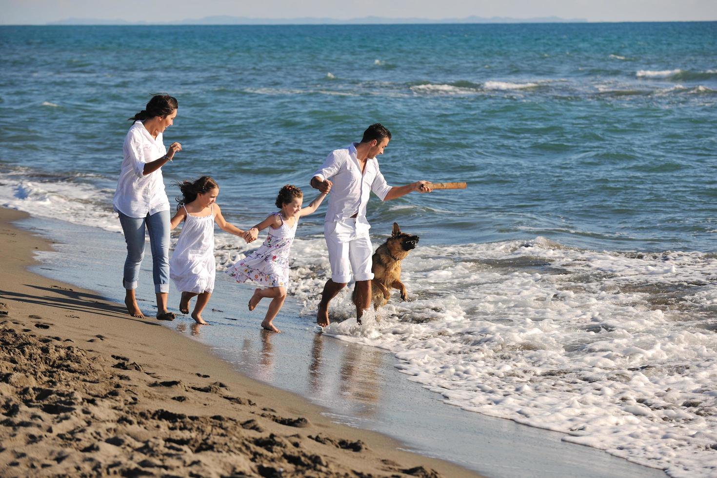 glückliche familie, die mit hund am strand spielt foto