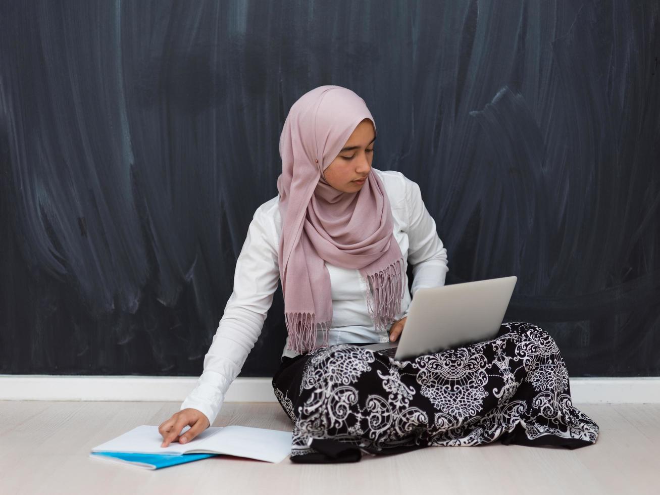 Arabischer Teenager mit Hijab, der auf dem Boden des Hauses sitzt und während der Coronavirus-Pandemie Online-Kurse anschaut. selektiver Fokus foto