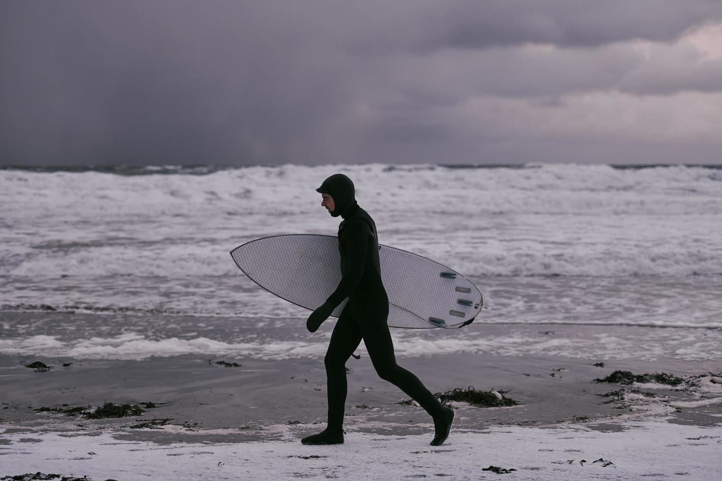 arktischer surfer, der nach dem surfen am strand vorbeigeht foto