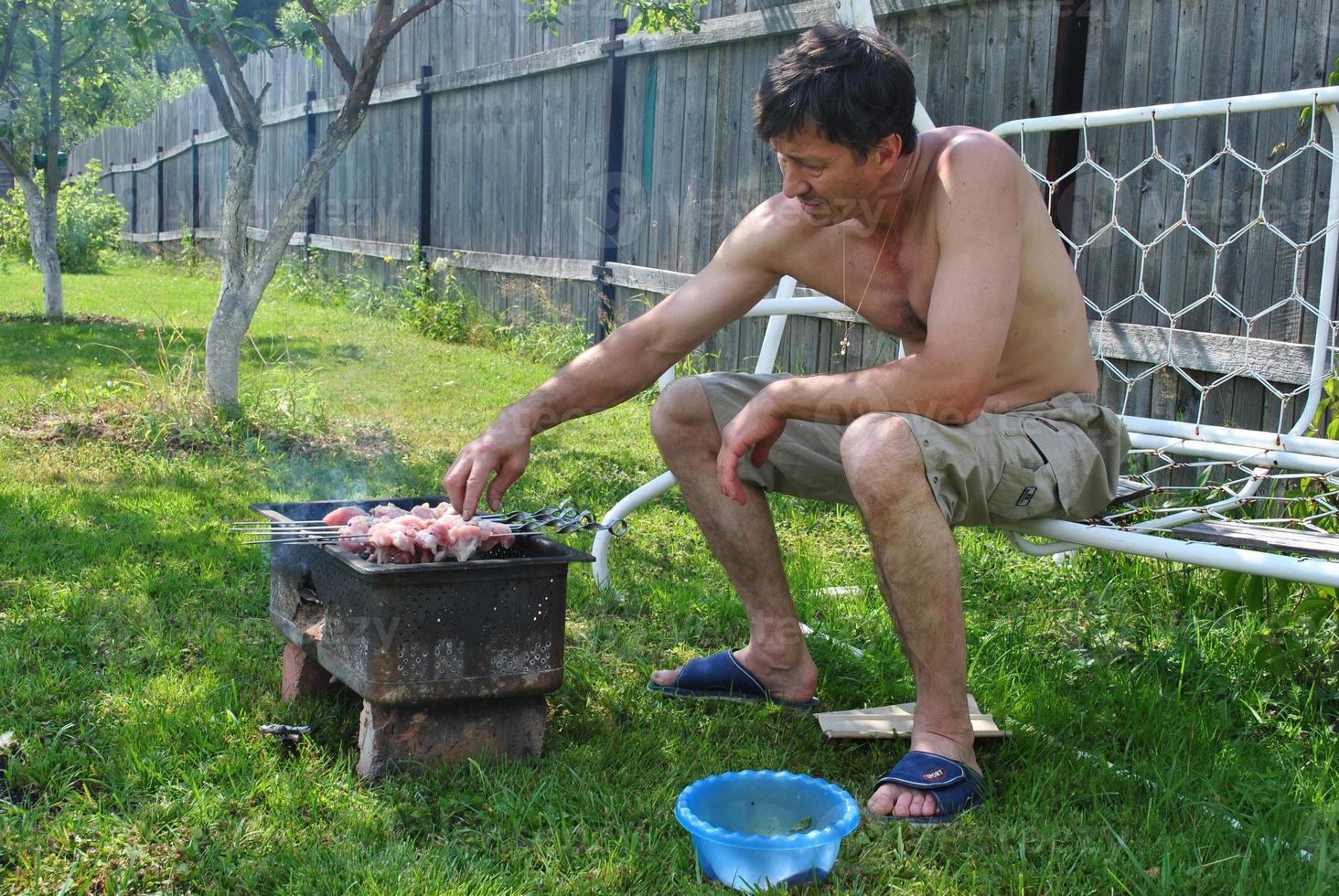 Ein Mann in Shorts kocht Fleisch auf dem Grill. foto