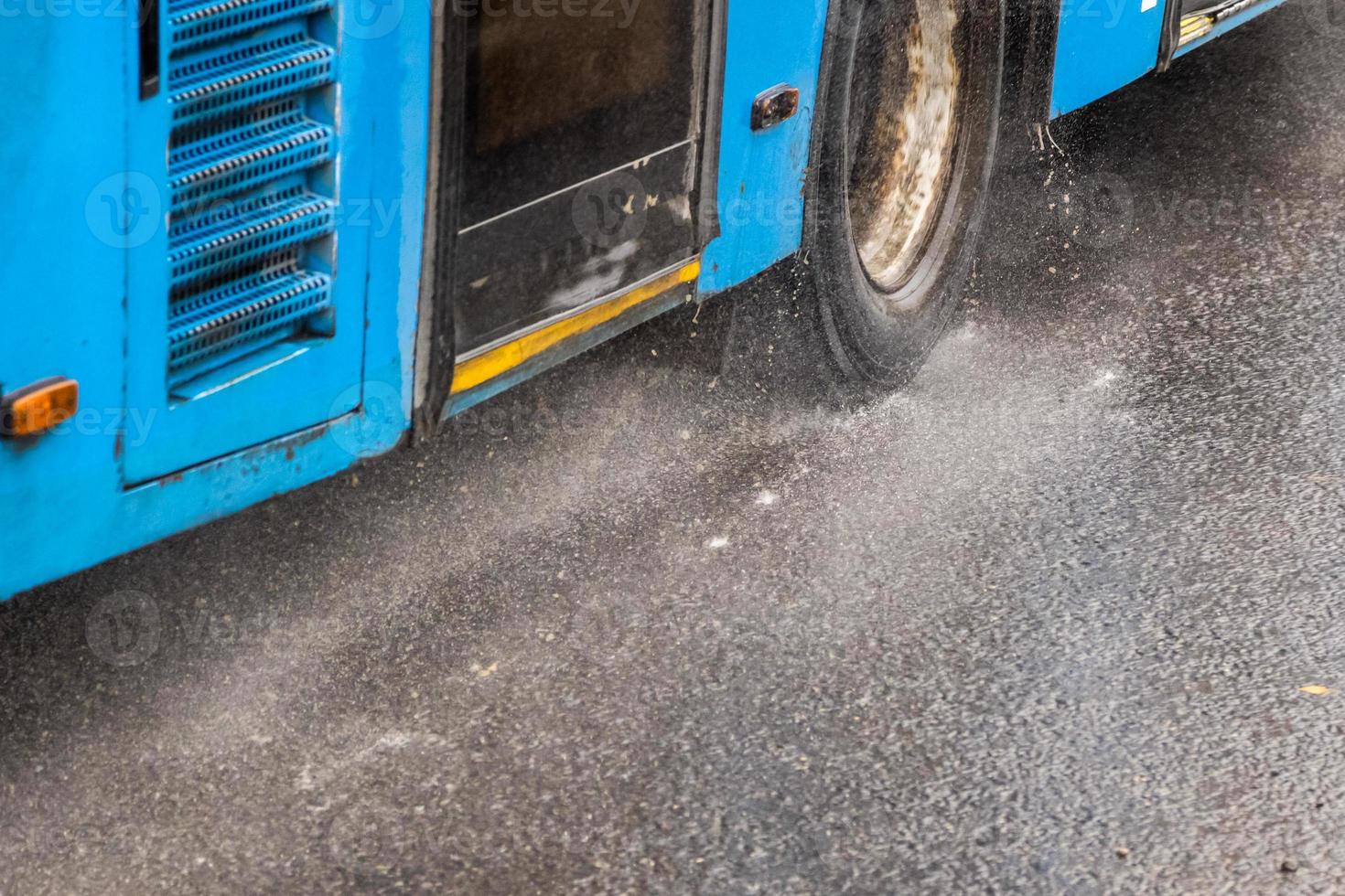 blauer stadtbus, der auf regnerischer straße mit wasserspritzern fährt foto