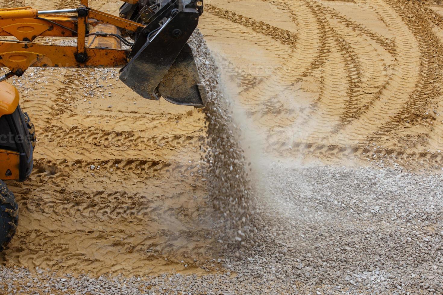 Ein Bulldozer schüttet auf einer Baustelle Kies aus einem Eimer auf den verdichteten Sand foto