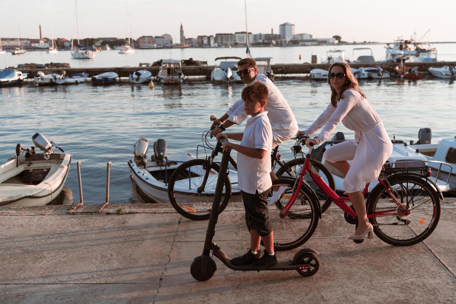 glückliche familie, die zusammen einen schönen morgen am meer genießt, eltern, die fahrrad fahren, und ihr sohn, der einen elektroroller fährt. selektiver Fokus foto