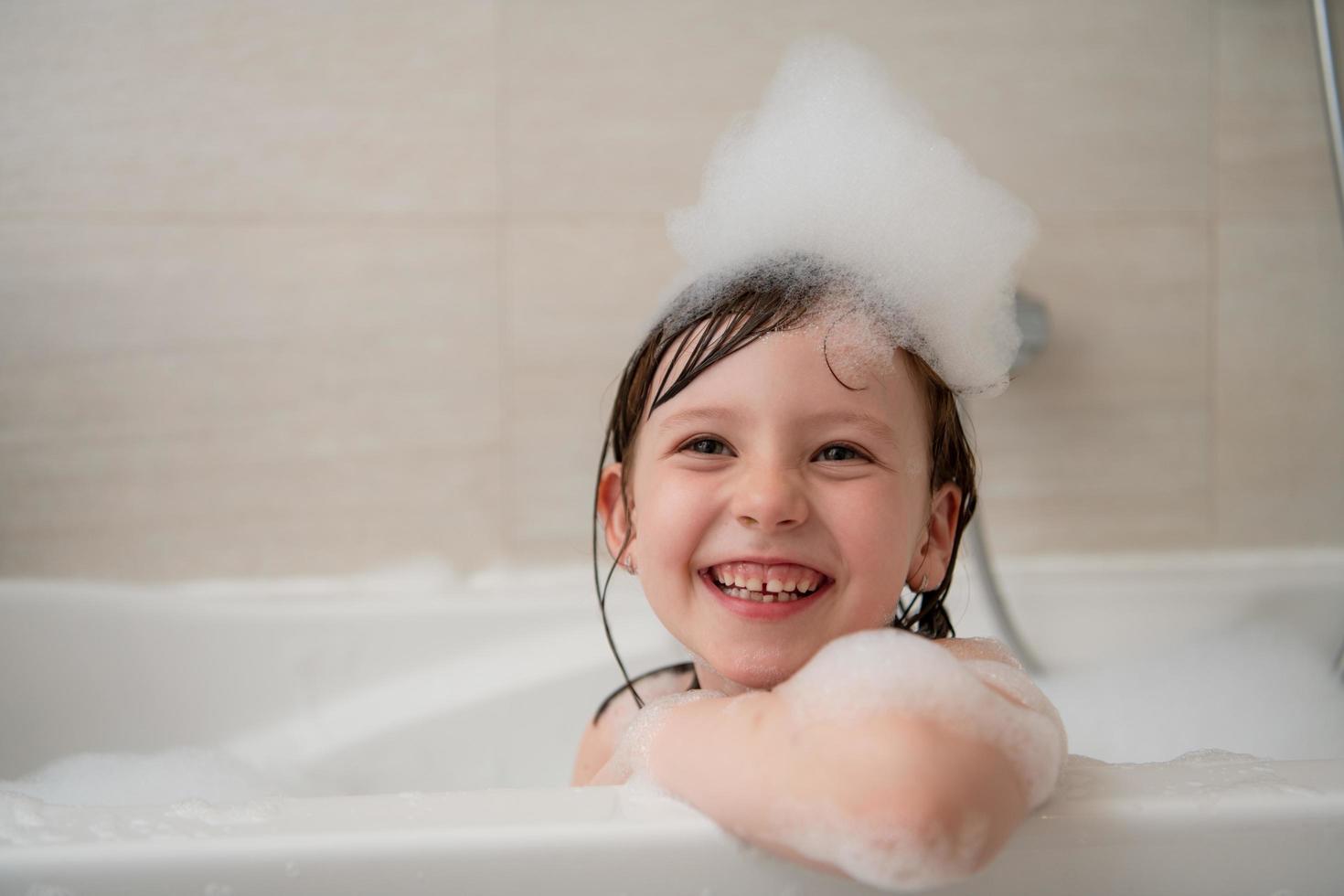 kleines Mädchen im Bad, das mit Schaum spielt foto